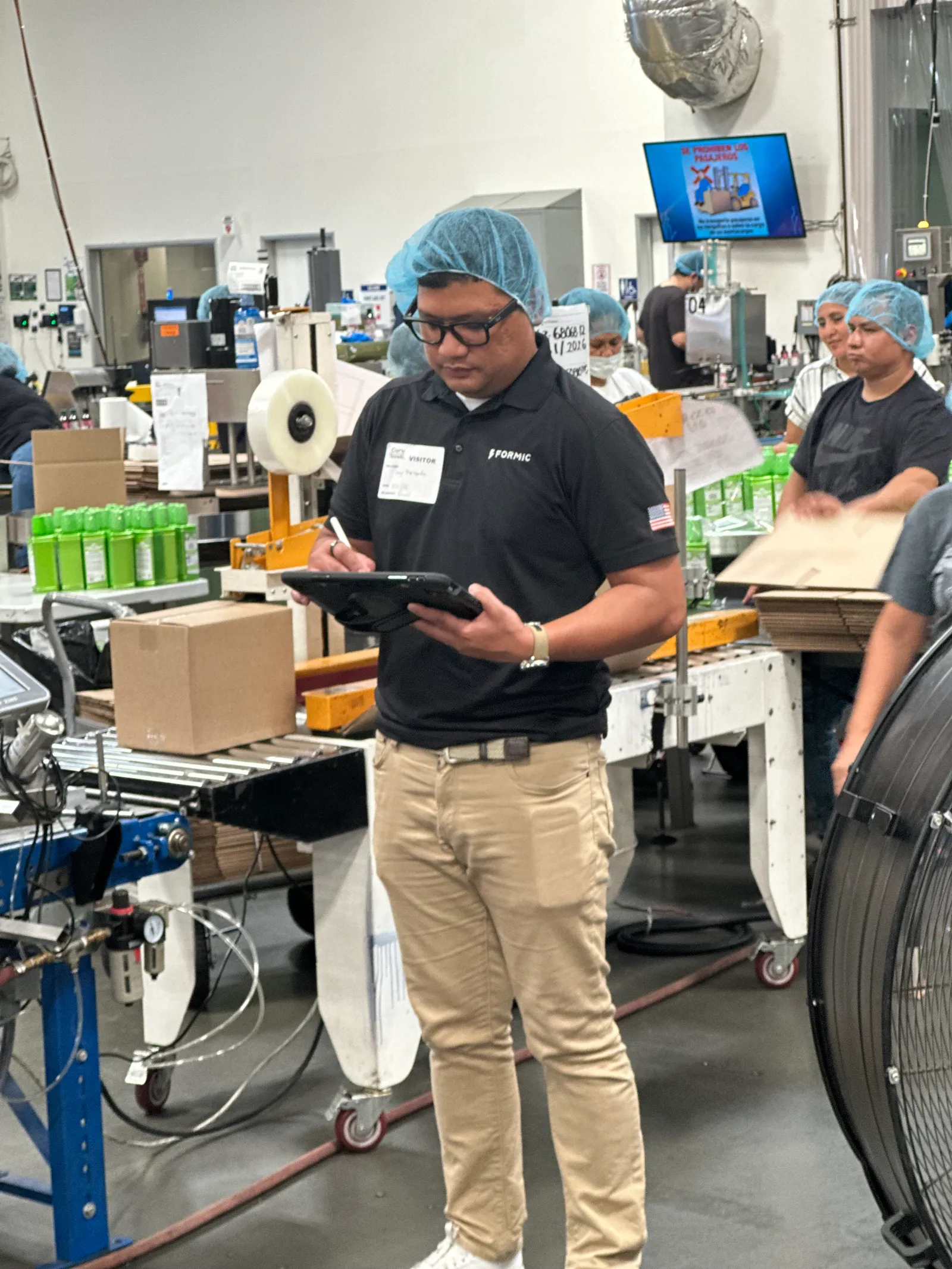 Dany Napitupulu taking notes on a tablet beside a running packaging line during an onsite assessment