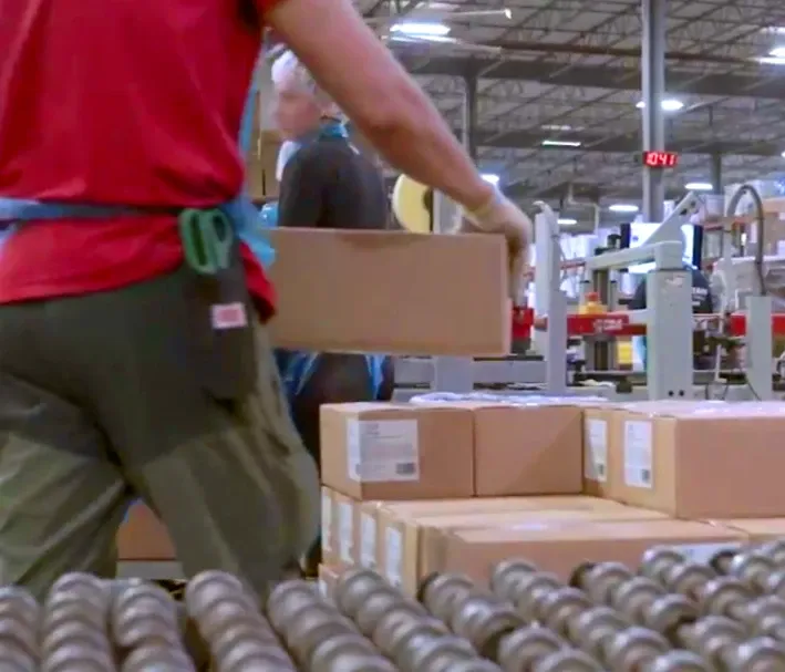Worker hand-carrying a taped case onto a growing stack, the repetitive palletizing job Formic Fast Track takes over