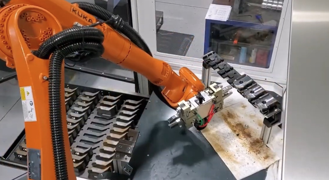 Orange KUKA robot arm tending a CNC, moving a machined part between a fixtured tray and the spindle | Formic tends most major CNC and lathe platforms