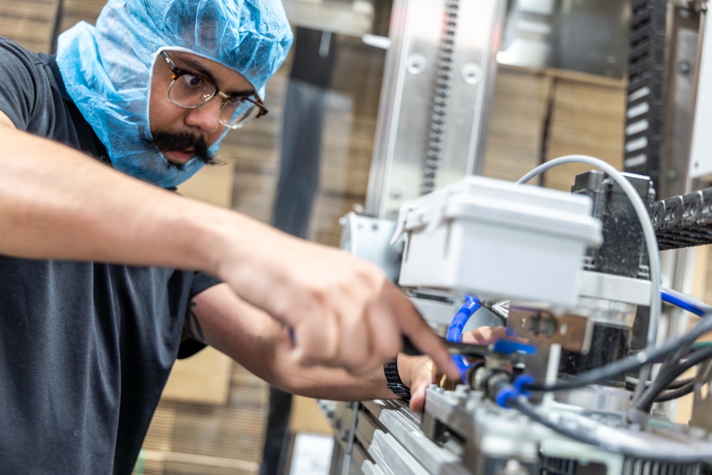 Operator in hairnet and safety glasses hands-on with a Formic case-packing cell, the skilled role Formic preserves while automating the high-turnover tasks around it