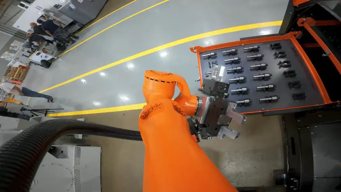The robot's own view, from a camera on the arm, carrying a loaded tray of shafts across the cell